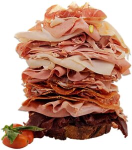 Towering sandwich piled with various deli meats and a side of lettuce and tomato.